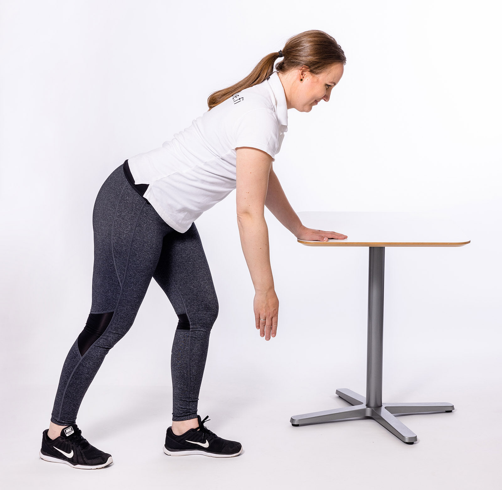 Nainen nojaa pöytään ja antaa toisen käden roikkua vapaana kohti lattiaa.